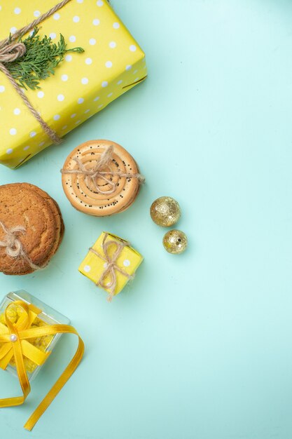 Vista vertical del estado de ánimo navideño con varias deliciosas galletas apiladas y una hermosa caja de regalo amarilla junto al accesorio de decoración en el lado derecho sobre fondo verde pastel