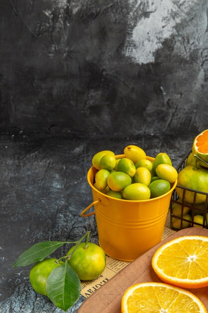 Vista vertical de frutas cítricas frescas con un cuchillo en la tabla de cortar de madera en el periódico sobre fondo gris