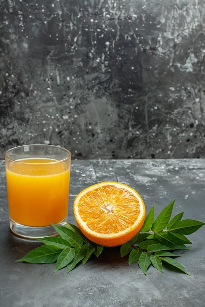 Vista vertical de la fuente de vitamina cortada naranjas frescas y jugo con hojas sobre fondo gris