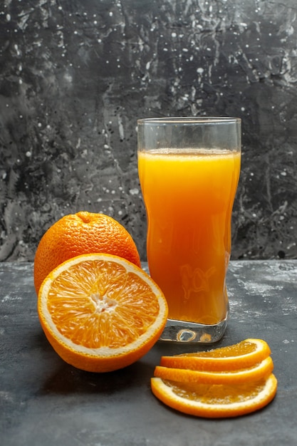 Vista vertical de la fuente de vitamina cortada naranjas frescas picadas y enteras y jugo sobre fondo gris