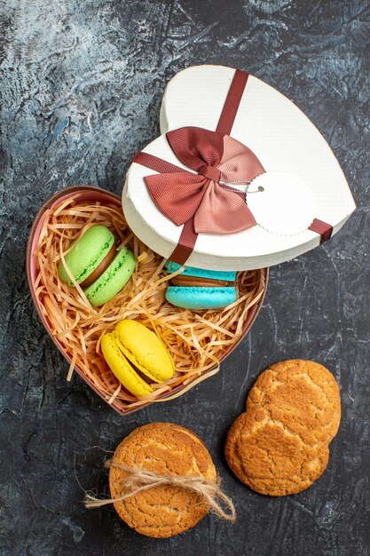 Vista vertical de una hermosa caja de regalo en forma de corazón con deliciosos macarons y galletas en un fondo oscuro y helado