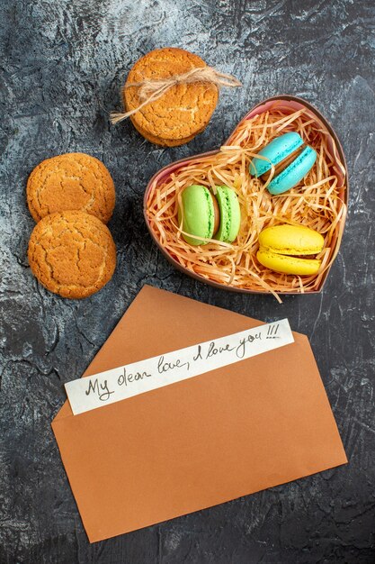 Vista vertical de la hermosa caja de regalo con macarons y sobres de galletas con carta de amor sobre fondo oscuro helado