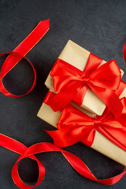 Vista vertical de hermosos regalos apilados con cinta roja sobre fondo oscuro