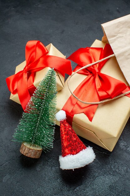 Vista vertical de hermosos regalos con cinta roja y árbol de navidad sombrero de santa claus en una mesa oscura