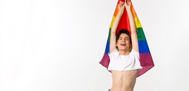 Vista vertical del hombre gay orgulloso y feliz levantando la bandera del arco iris lgbtq sonriendo con emoción aliviada