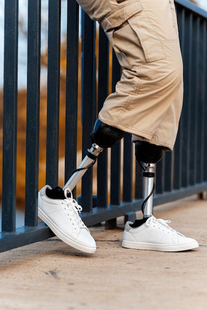 Foto gratuita vista vertical de un hombre con piernas ortopédicas y zapatillas blancas descansó un pie en la cerca