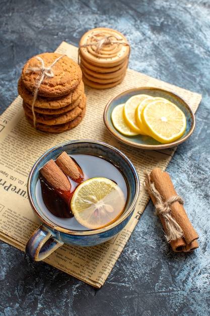 Vista vertical de la hora del té con deliciosas galletas apiladas canela limón en un periódico viejo sobre fondo oscuro