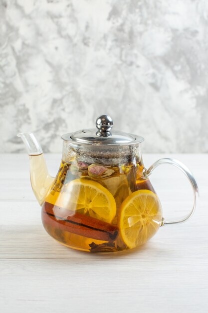 Vista vertical de la hora del té con té de hierbas mezclado con limón en una olla de vidrio sobre mesa blanca