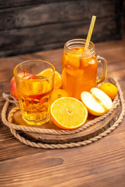 Vista vertical de jugo fresco orgánico en una botella y vaso servido con tubo y frutas sobre una tabla para cortar y sobre una mesa de madera marrón