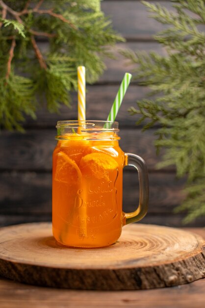 Vista vertical de jugo de naranja fresco en un vaso con tubo en una bandeja de madera sobre fondo marrón