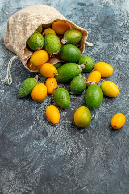 Vista vertical de kumquats frescos dentro y fuera de una pequeña bolsa blanca caída sobre fondo gris