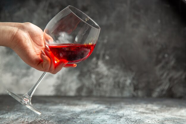Vista vertical de la mano de la mujer sosteniendo un vaso de vino tinto seco sobre fondo gris