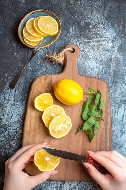 Vista vertical de una mano para picar limones frescos y menta sobre una tabla de cortar de madera sobre fondo oscuro