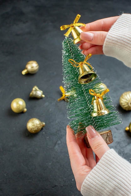 Vista vertical de la mano que sostiene el árbol de navidad y accesorios de decoración sobre fondo oscuro