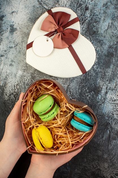 Foto gratuita vista vertical de la mano que sostiene la caja de regalo en forma de corazón sobre fondo helado oscuro