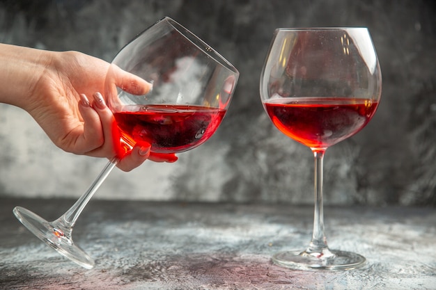 Vista vertical de la mano que sostiene una de las copas de vino tinto seco sobre fondo gris