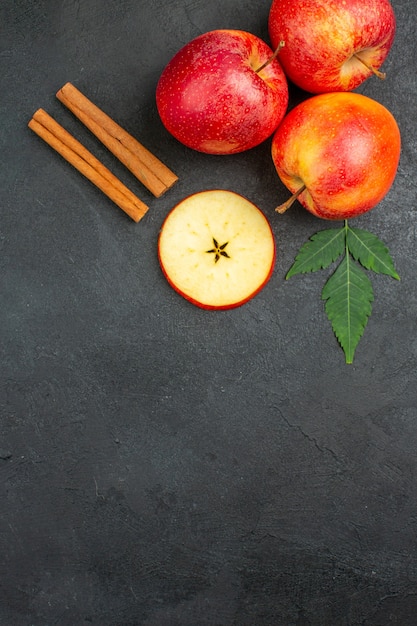 Foto gratuita vista vertical de manzanas rojas orgánicas naturales frescas enteras y cortadas con hojas verdes limones canela sobre fondo negro