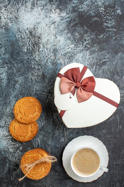 Vista vertical de la mejor sorpresa con una hermosa caja de regalo y una taza de galletas de café para su amado sobre fondo oscuro helado