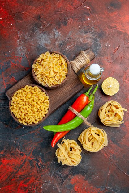 Vista vertical de pastas crudas pimientos de cayena atados entre sí con una botella de aceite de cuerda limón o ajo sobre fondo de colores mezclados