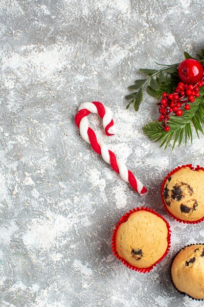 Vista vertical de pequeños cupcakes, dulces y ramas de abeto, accesorios de decoración, cono de coníferas en el lado derecho sobre la superficie del hielo