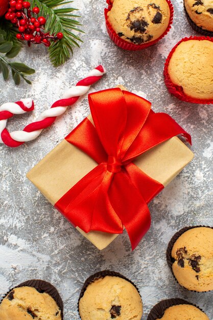 Vista vertical de pequeños cupcakes regalos de Navidad con cinta roja y ramas de abeto de caramelo en la mesa de hielo