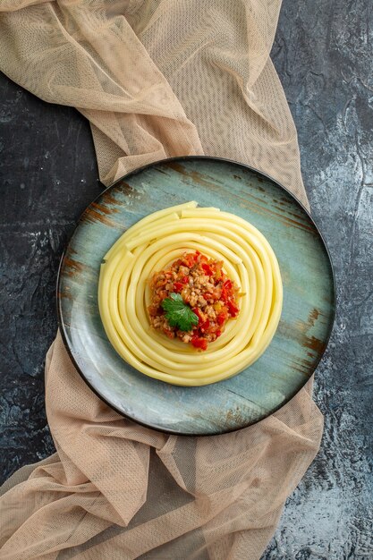 Vista vertical de una placa azul con una sabrosa comida de pasta servida con tomate y carne en una toalla de color bronceado