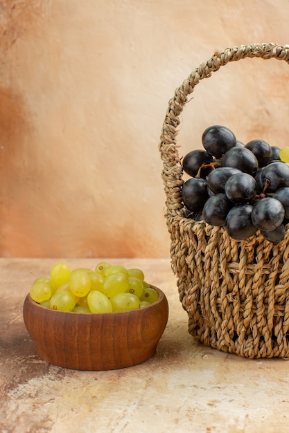 Vista vertical de racimos de uvas amarillas y negras en una canasta de madera y en una pequeña olla marrón