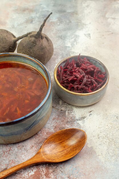 Vista vertical de remolacha fresca y sopa de borscht en una olla junto a la sopa de madera sobre fondo gris