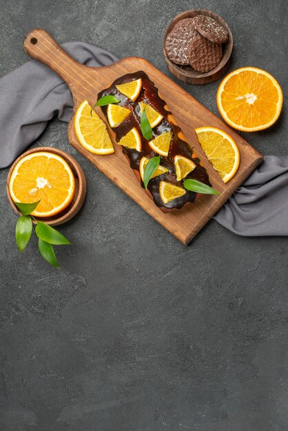 Vista vertical de sabrosos pasteles cortan limones con galletas en la tabla de cortar en imágenes de mesa oscura