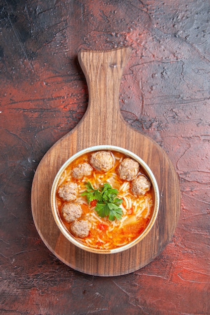 Foto gratuita vista vertical de sopa de albóndigas de tomate con fideos en un recipiente marrón sobre fondo oscuro