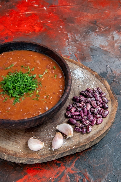 Vista vertical de la sopa de tomate, frijoles, ajo sobre tabla de cortar de madera sobre fondo de color de mezcla