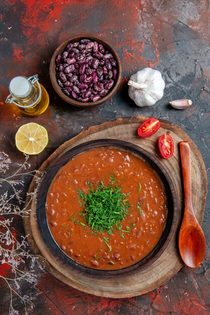 Vista vertical de la sopa de tomate en un recipiente marrón botella de aceite de frijoles y cuchara en la mesa de colores mezclados