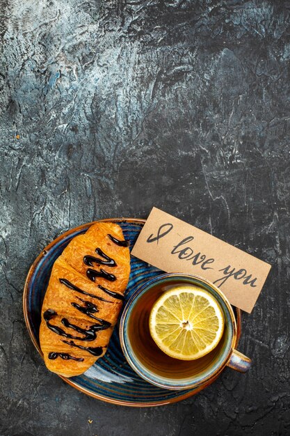 Vista vertical de una taza de té negro delicioso croisasant para amado en mesa oscura