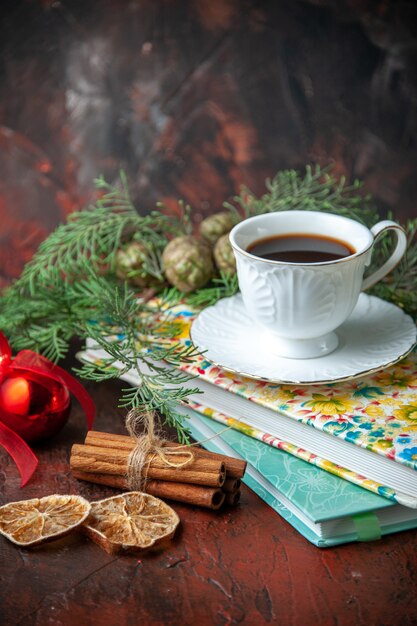 Vista vertical de una taza de té negro en dos libros, canela, limas y accesorios de decoración de ramas de abeto sobre fondo oscuro