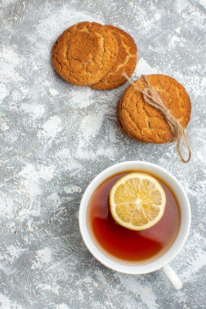 Vista vertical de una taza de té negro con limón y deliciosas galletas sobre la superficie del hielo