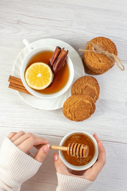 Vista vertical de té negro con limón y canela limas miel galletas apiladas sobre fondo blanco.