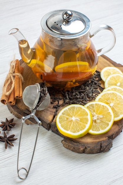 Vista vertical de té negro con limones limón y canela en una bandeja de madera sobre fondo blanco.