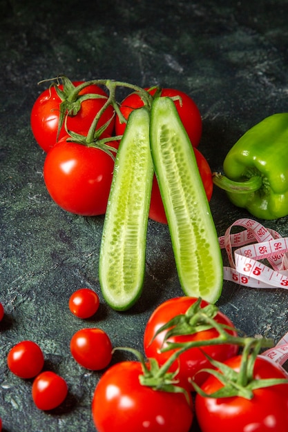 Vista vertical de tomates frescos, pimientos y pepinos medidores en la superficie de colores oscuros con espacio libre