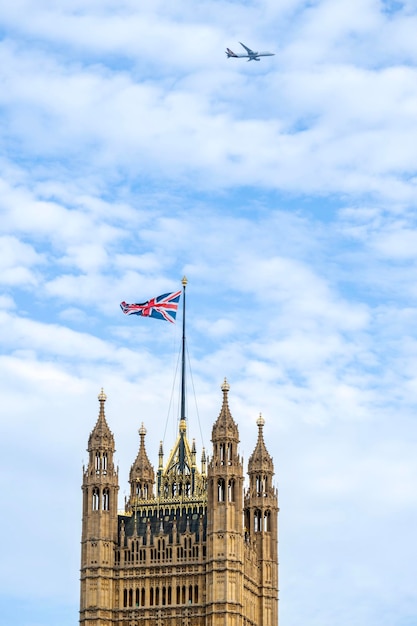 Foto gratuita vista vertical de la torre victoria ubicada en el palacio de westminster en el centro de londres reino unido cielo azul con avión volando en el fondo