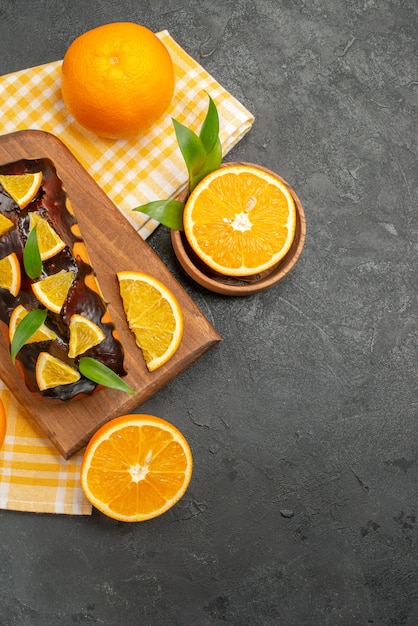 Vista vertical de tortas blandas enteras y limones cortados con hojas en la mesa oscura