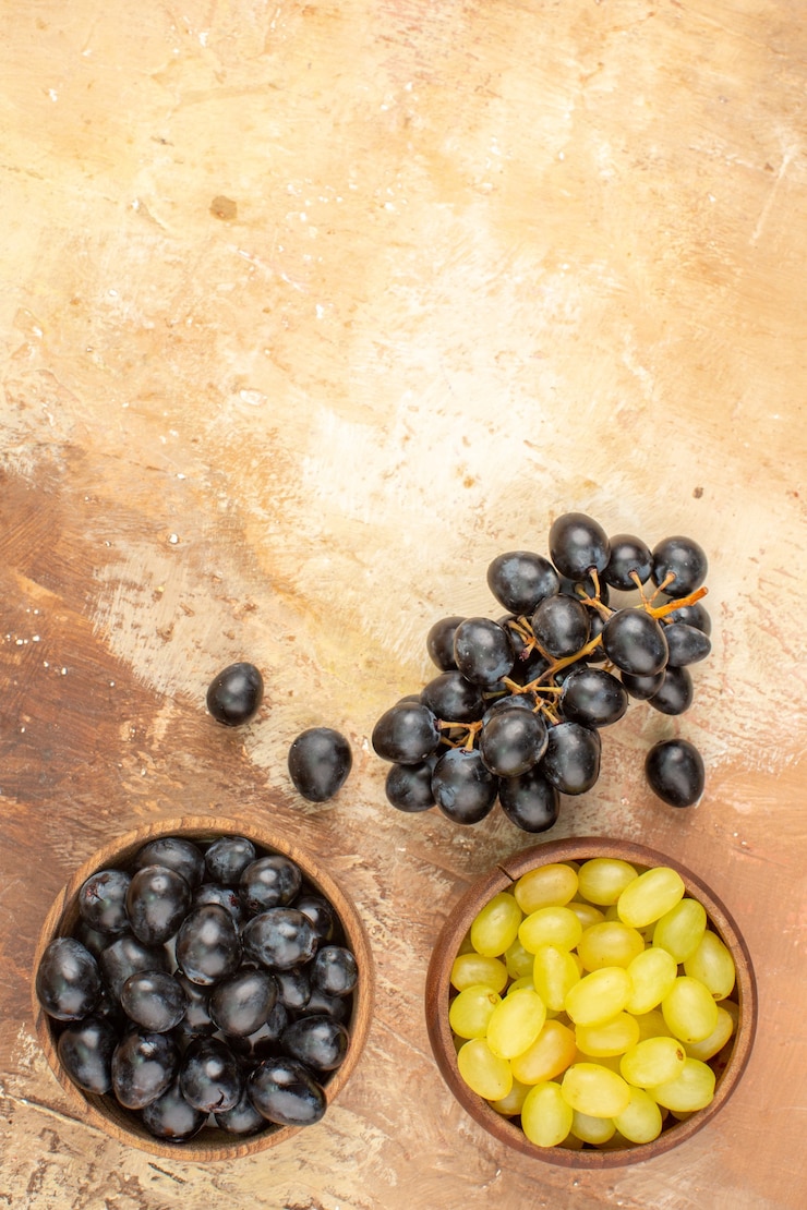 Foto gratuito vista vertical de uvas frescas negras y amarillas en pequeñas macetas de madera marrón y