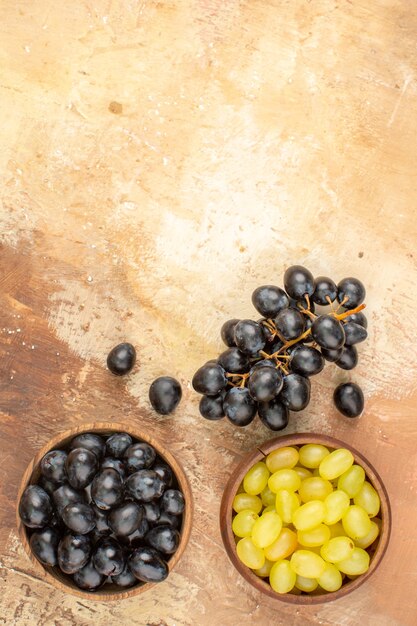 Vista vertical de uvas frescas negras y amarillas en pequeñas macetas de madera marrón y