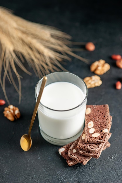 Foto gratuita vista vertical de un vaso de leche y galletas de chocolate cuchara dorada cacahuetes nueces sobre superficie negra