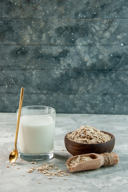 Vista vertical del vaso lleno de leche y avena dentro y fuera de la olla marrón sobre fondo gris