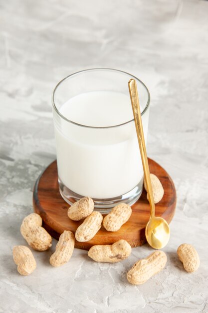 Vista vertical del vaso lleno de leche en bandeja de madera y cuchara de frutos secos sobre fondo blanco.