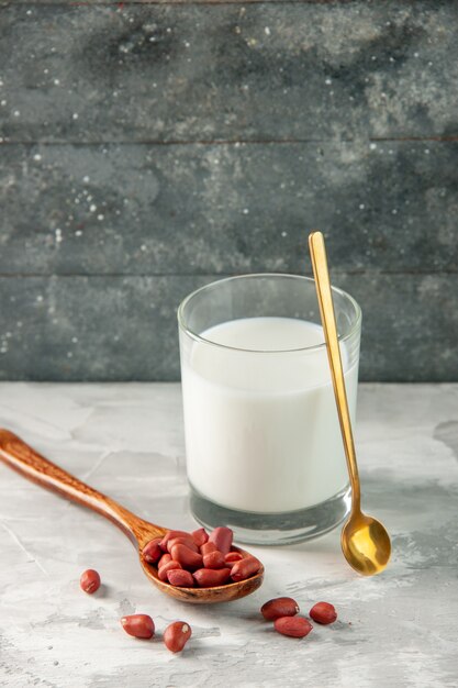 Vista vertical del vaso lleno de leche y cacahuetes en cuchara sobre fondo gris