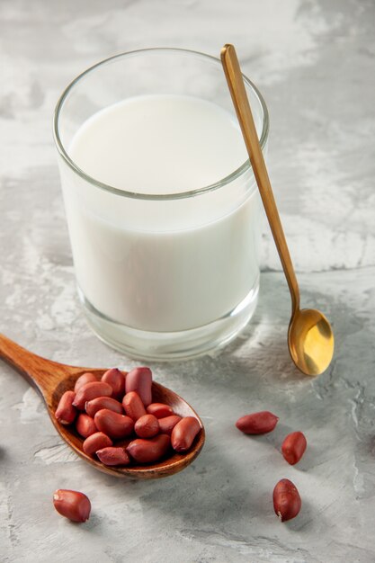 Vista vertical del vaso lleno de leche y cacahuetes en cuchara sobre fondo gris