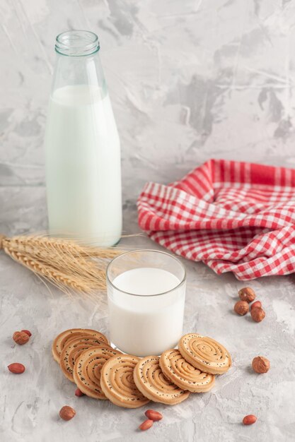 Vista vertical del vaso lleno de leche y galletas, maní, espigas, toalla despojada de rojo sobre la superficie blanca manchada
