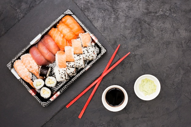 Vívidos rollos de pescado asiático en bandeja y palillos con salsa de soja y wasabi sobre piso de concreto