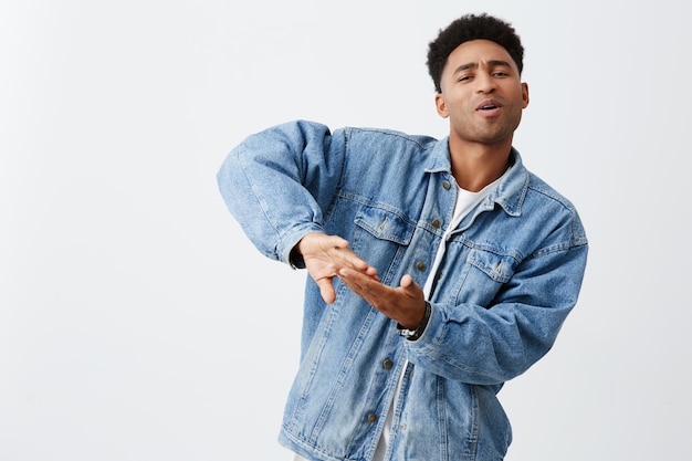 Viviendo una vida rica. Emociones positivas. Retrato de joven atractivo hombre de piel negra con peinado afro en camiseta blanca y chaqueta de mezclilla tirando dinero para video clip, divirtiéndose con amigos